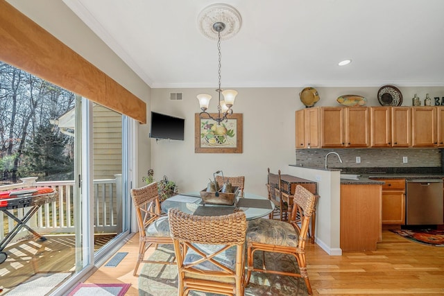 kitchen with crown molding, tasteful backsplash, an inviting chandelier, light wood-style floors, and a sink