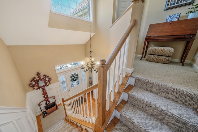 stairs featuring a wainscoted wall, a high ceiling, a decorative wall, and an inviting chandelier