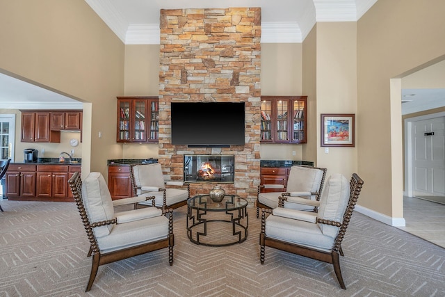 living area featuring light colored carpet, a fireplace, a towering ceiling, baseboards, and ornamental molding