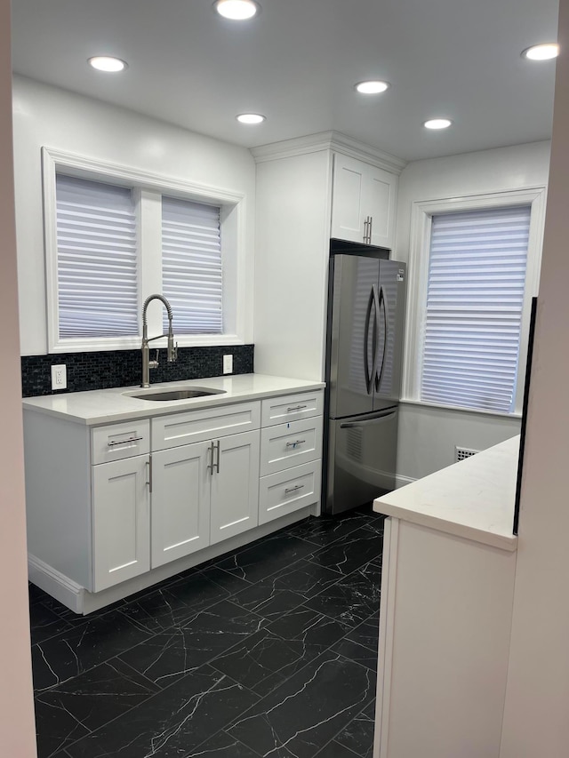 kitchen featuring light countertops, freestanding refrigerator, white cabinetry, and a sink