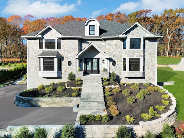 french country home featuring stone siding, french doors, a front lawn, and a shingled roof