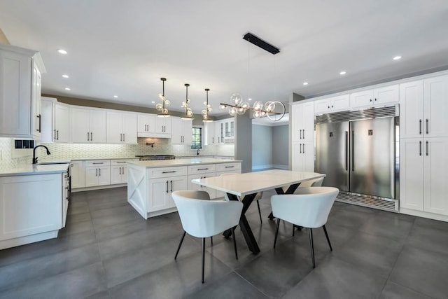 kitchen featuring a center island, light countertops, stainless steel built in refrigerator, white cabinetry, and backsplash