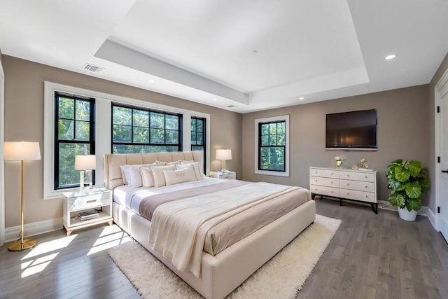 bedroom with wood finished floors, a raised ceiling, visible vents, and baseboards