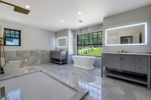 bathroom with a wealth of natural light, visible vents, tile walls, and vanity