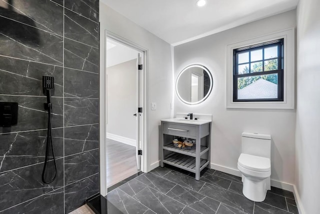 bathroom featuring toilet, baseboards, a tile shower, and vanity