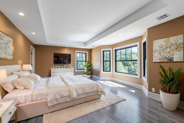 bedroom with a tray ceiling, recessed lighting, visible vents, wood finished floors, and baseboards