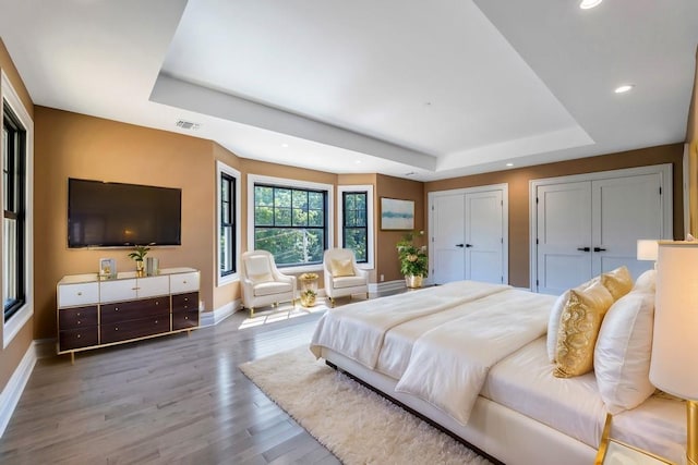 bedroom featuring multiple closets, visible vents, a tray ceiling, and wood finished floors