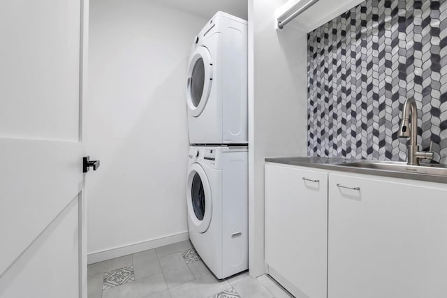 laundry room with light tile patterned floors, cabinet space, a sink, stacked washing maching and dryer, and baseboards