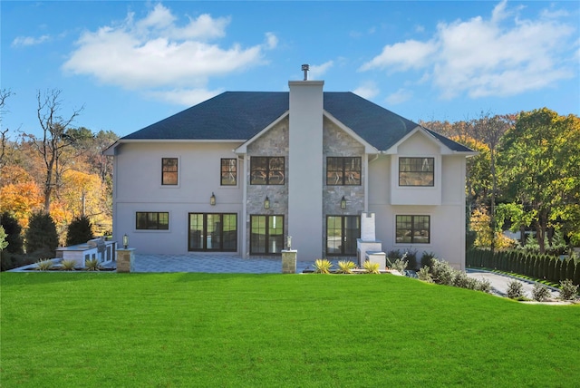 back of house featuring a yard, a chimney, a patio area, fence, and stone siding