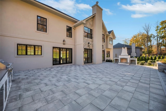 back of house with a patio area, a chimney, an outdoor fireplace, and stucco siding