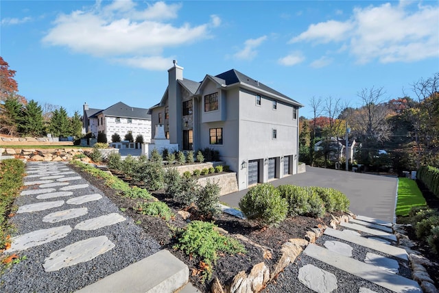 view of side of home with aphalt driveway, a chimney, an attached garage, and stucco siding