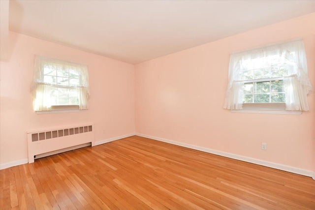 spare room with radiator, light wood-style flooring, and baseboards