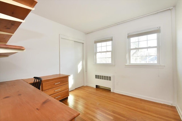 unfurnished office featuring a healthy amount of sunlight, light wood finished floors, radiator heating unit, and baseboards