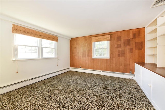 empty room with baseboard heating, plenty of natural light, visible vents, and wooden walls