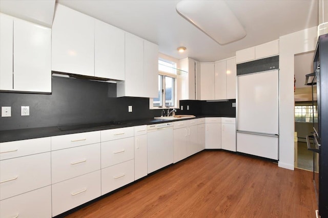 kitchen with black electric stovetop, dark countertops, white dishwasher, a sink, and paneled fridge