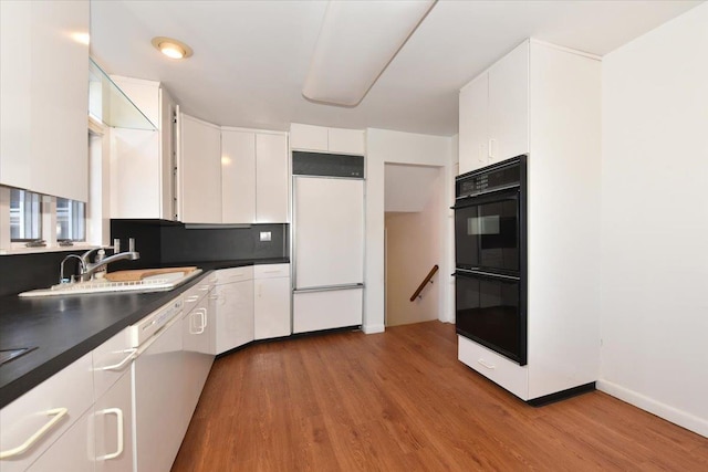 kitchen with dobule oven black, white cabinets, dark countertops, a sink, and built in fridge