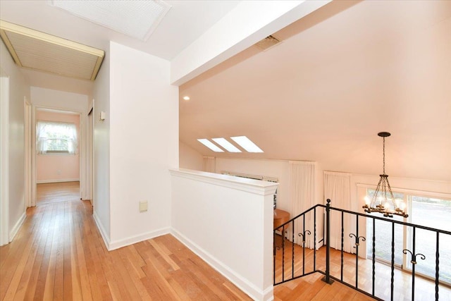 corridor with baseboards, light wood-style flooring, an upstairs landing, and an inviting chandelier