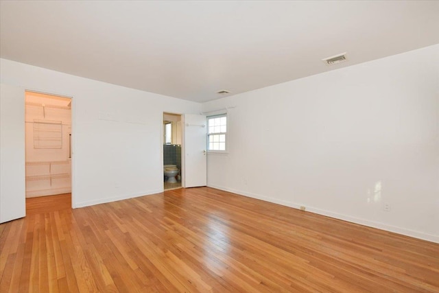 empty room with light wood finished floors, visible vents, and baseboards