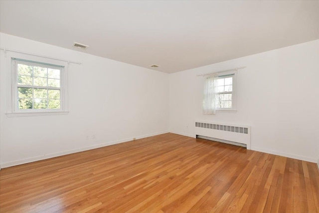 unfurnished room with radiator heating unit, light wood-type flooring, visible vents, and baseboards