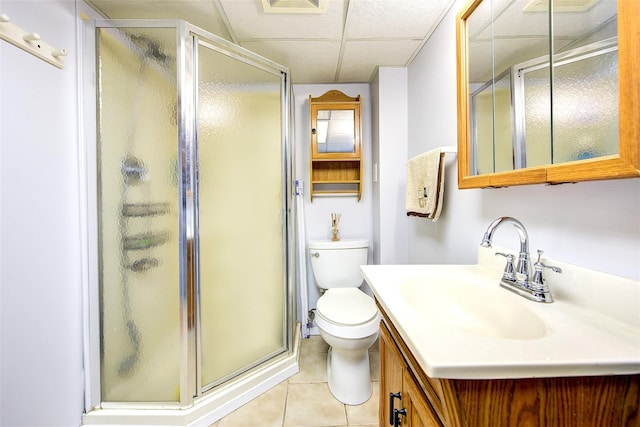 bathroom featuring a drop ceiling, toilet, vanity, a shower stall, and tile patterned floors