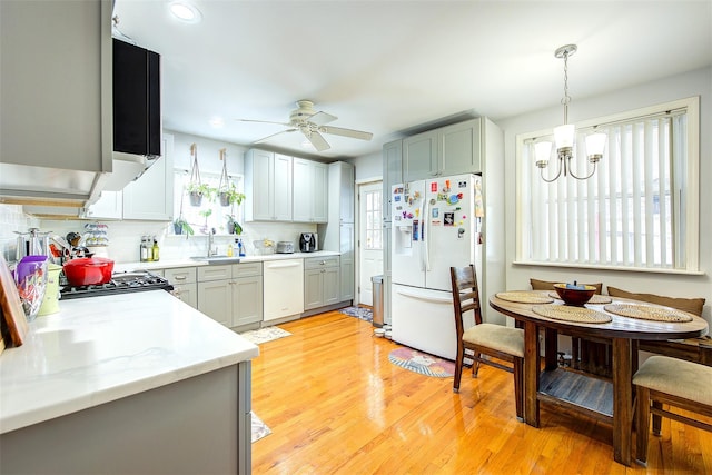 kitchen with white appliances, tasteful backsplash, light wood finished floors, decorative light fixtures, and a sink