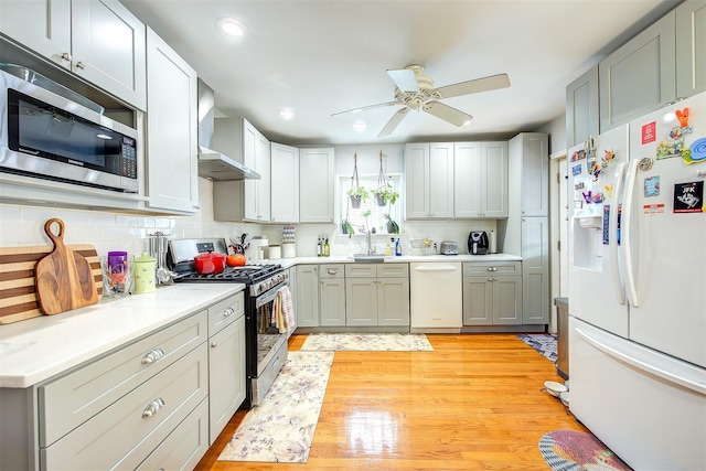 kitchen featuring stainless steel appliances, a sink, light countertops, wall chimney range hood, and decorative backsplash