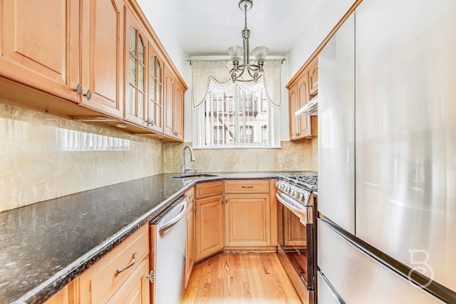 kitchen featuring dark stone counters, glass insert cabinets, appliances with stainless steel finishes, pendant lighting, and a sink