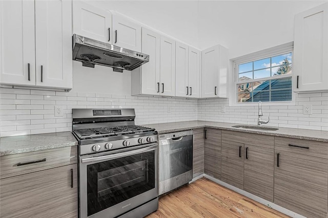 kitchen with light stone countertops, under cabinet range hood, appliances with stainless steel finishes, and white cabinets