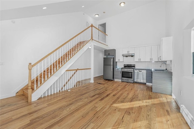 kitchen with high vaulted ceiling, under cabinet range hood, stainless steel appliances, a sink, and white cabinetry