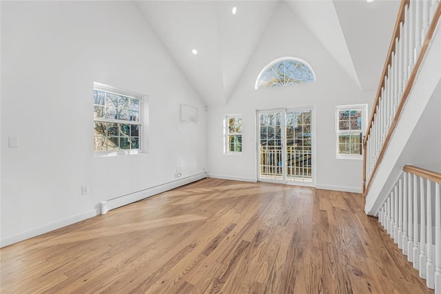 empty room with high vaulted ceiling, a baseboard heating unit, baseboards, stairs, and light wood-type flooring