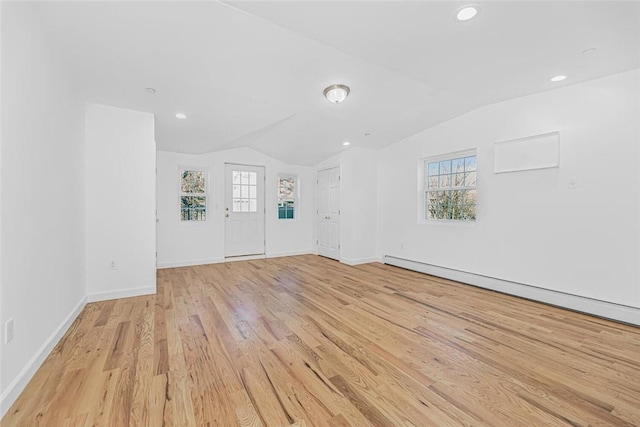 interior space featuring light wood-style floors, baseboard heating, vaulted ceiling, and a wealth of natural light