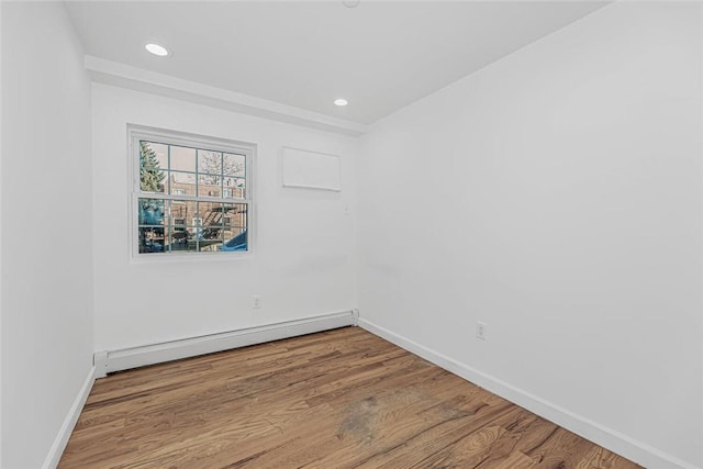 spare room featuring a baseboard radiator, baseboards, wood finished floors, and recessed lighting