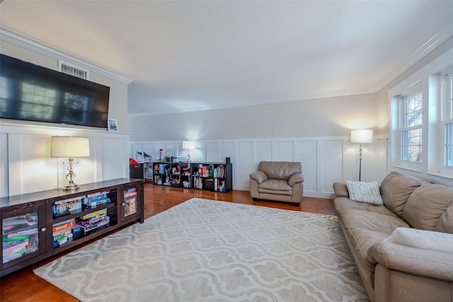 living room featuring a wainscoted wall, visible vents, a decorative wall, ornamental molding, and wood finished floors