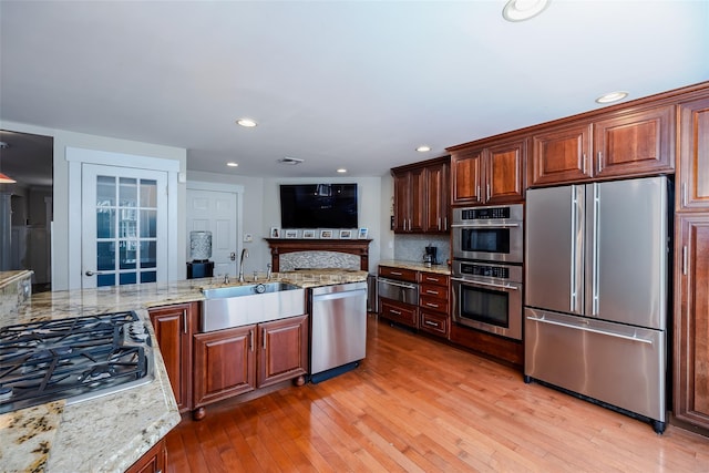 kitchen featuring light stone countertops, light wood-style flooring, stainless steel appliances, and a sink