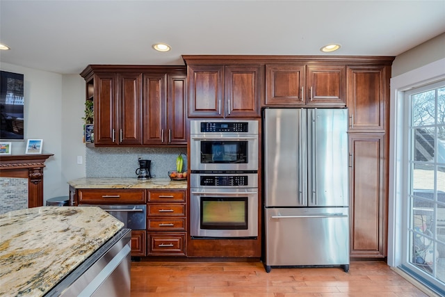 kitchen with stainless steel appliances, recessed lighting, decorative backsplash, light wood-style floors, and light stone countertops