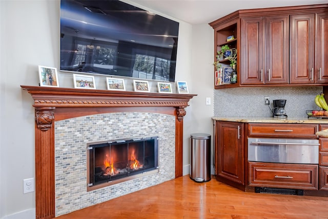 bar with a warming drawer, light wood finished floors, a tiled fireplace, and decorative backsplash