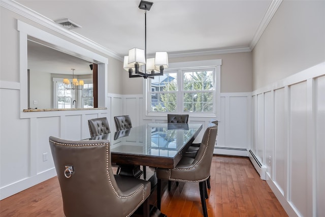 dining space with crown molding, hardwood / wood-style floors, a decorative wall, and a notable chandelier