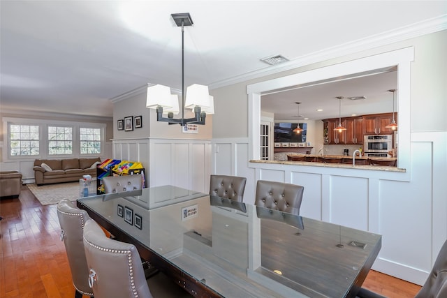 dining area with visible vents, a decorative wall, crown molding, and wood finished floors