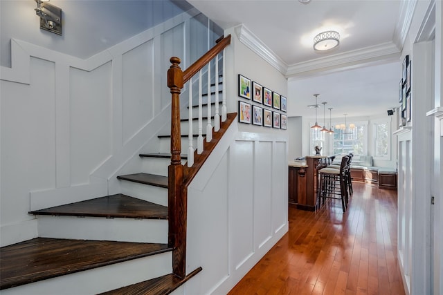 stairs with crown molding, a decorative wall, an inviting chandelier, and wood finished floors