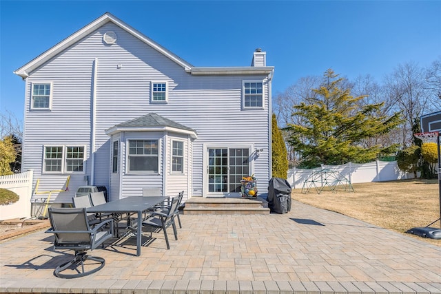 rear view of property with outdoor dining area, a patio area, fence, and a chimney