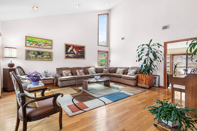 living area with light wood finished floors, visible vents, and high vaulted ceiling