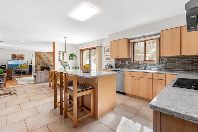 kitchen featuring light brown cabinetry, black electric stovetop, a stone fireplace, stainless steel dishwasher, and a sink