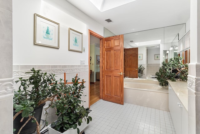 bathroom with tile walls, visible vents, a bath, and wainscoting