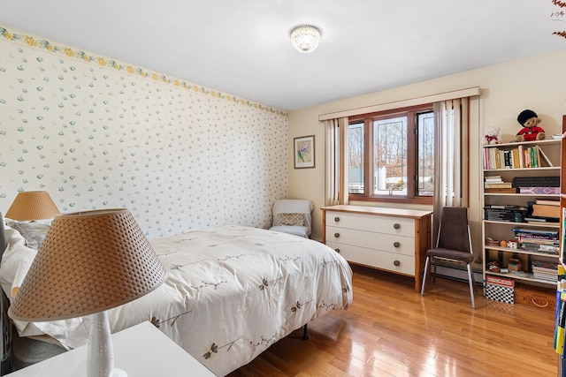 bedroom with hardwood / wood-style floors, baseboard heating, and wallpapered walls