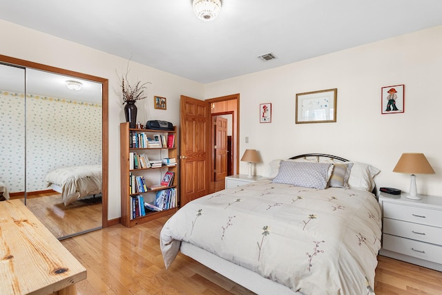 bedroom with light wood-type flooring, baseboards, visible vents, and a closet