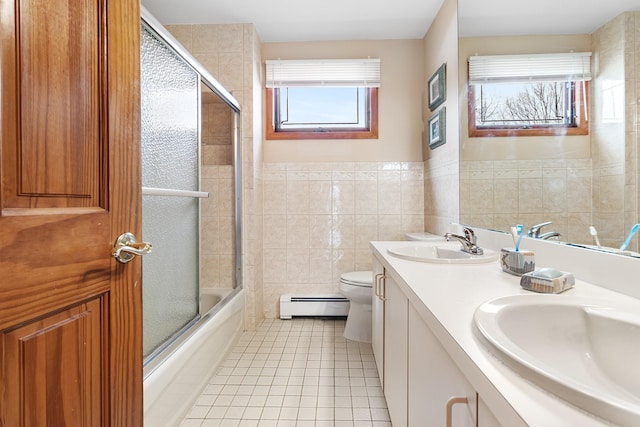 full bath with tile walls, toilet, a baseboard heating unit, a sink, and tile patterned floors