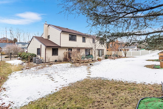 snow covered property with a chimney, fence, and cooling unit