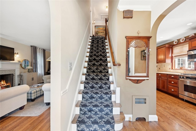 staircase featuring arched walkways, crown molding, radiator heating unit, wood finished floors, and a tile fireplace