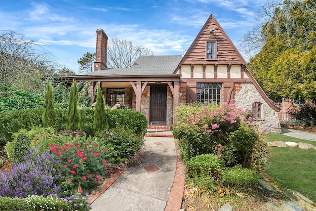 tudor home featuring stone siding, a chimney, brick siding, and roof with shingles