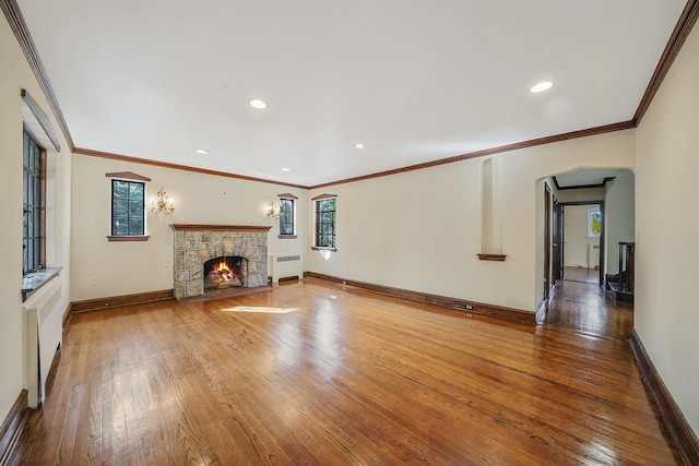 unfurnished living room with baseboards, hardwood / wood-style flooring, radiator heating unit, crown molding, and a stone fireplace